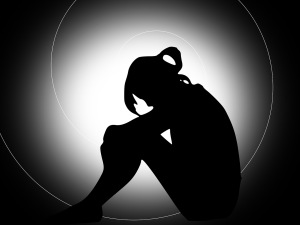 Silhouette of a woman sitting with her knees drawn up, surrounded by a soft gray spiral on a black background, symbolising introspection and solitude.