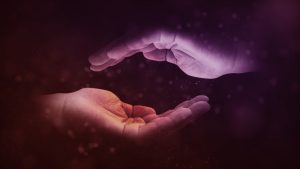 Two hands cupped, holding space, lit in purple and orange on a dark background, illustrating connection, shared support, and the therapeutic alliance. 