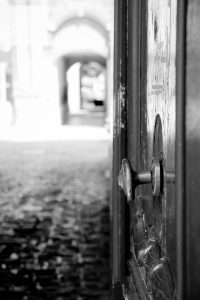 Black and white image of an open door with an out of focus background, suggesting curiosity and stepping into reflection. 