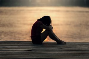 Woman sitting alone on a jetty at sunset representing the loneliness of IVF and fertility struggles.
