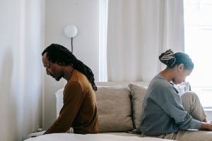 Couple sitting back to back on a bed, physically close, but emotionally distant, representing loneliness within the relationship.